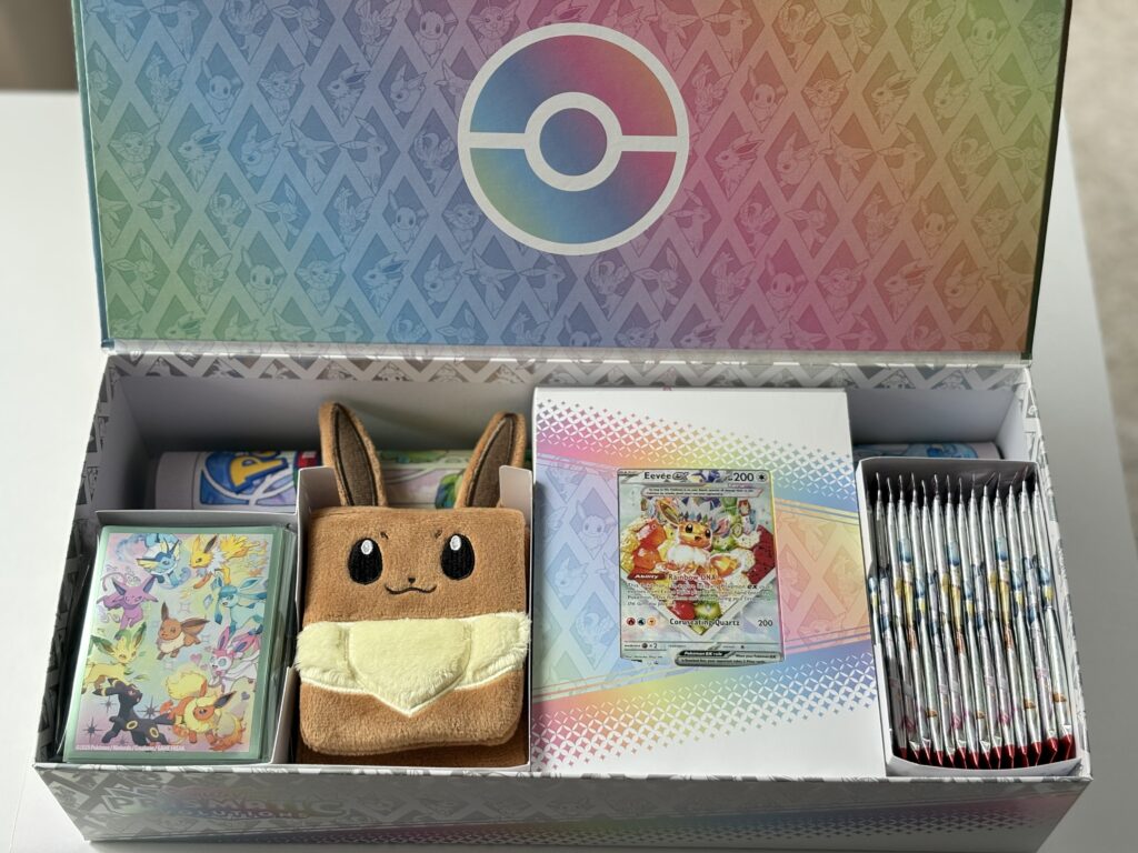Otwarte pudełko z widocznymi 15 boosterami, promo Eevee ex, deck boxem, matą oraz koszulkami