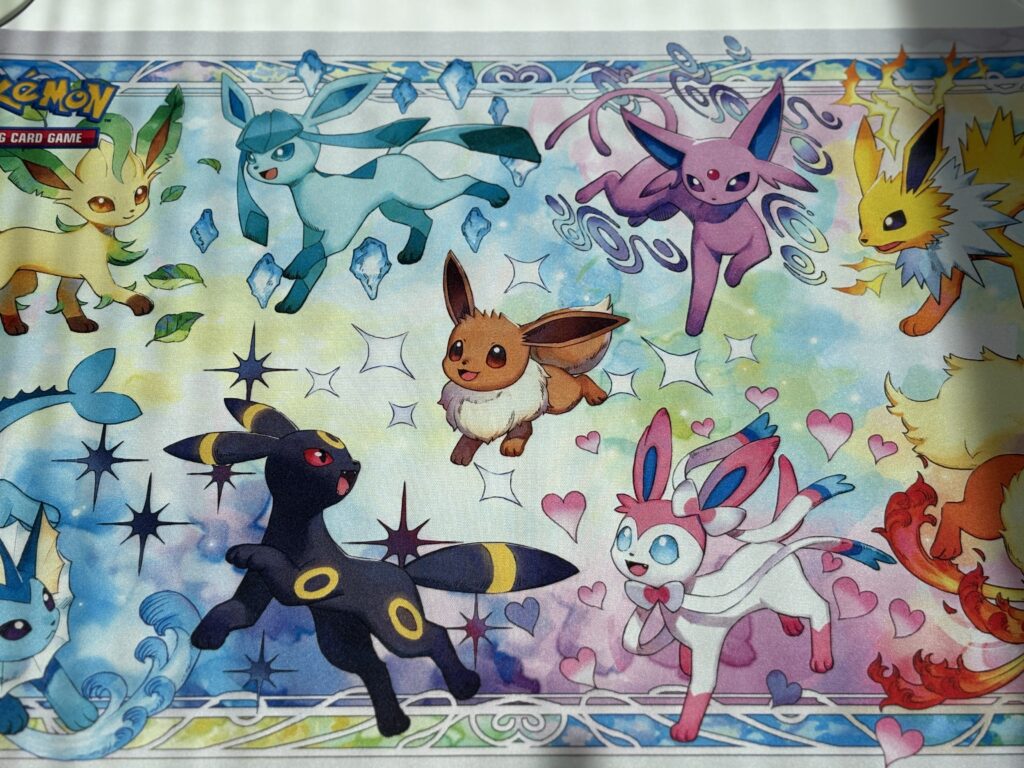 Mata do gry z zestawu Prismatic Evolutions – przedstawia Eevee i jego ewolucje, kolorowa i duża